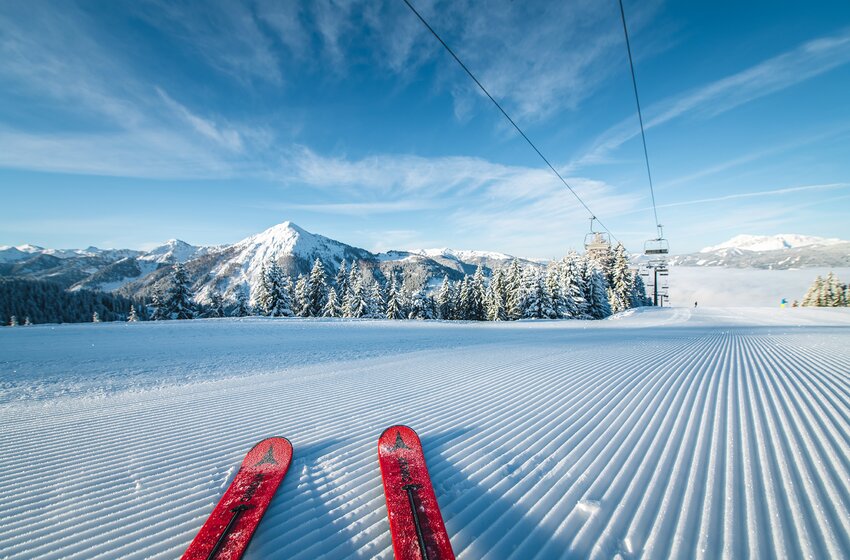Red skis on freshly groomed slope with view of snowy mountains and clear blue sky. | © Salzburger Sportwelt Amadé GmbH