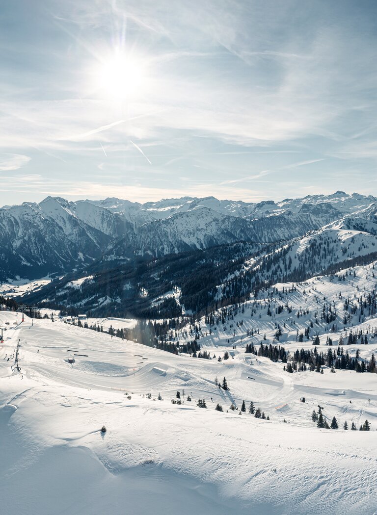 Wide winter landscape with snowy slopes, ski runs, sunshine and mountain panorama under lightly clouded sky. | © SHUTTLEBERG GmbH & Co KG