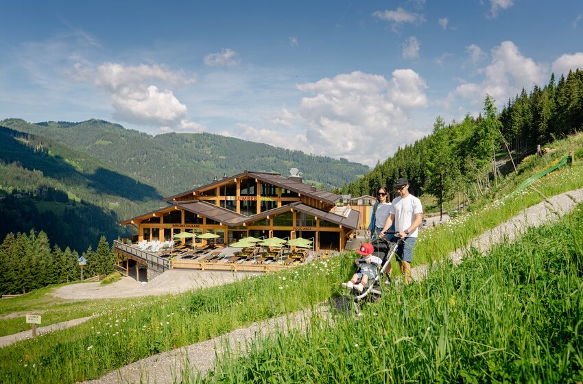 Familie mit Kinderwagen spaziert oberhalb des Lumberjack-Restaurants am Hang | © SHUTTLEBERG GmbH & Co KG