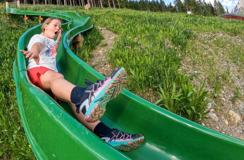 Child with open mouth sliding fast on green curved slide in grassy hillside | © SHUTTLEBERG GmbH & Co KG