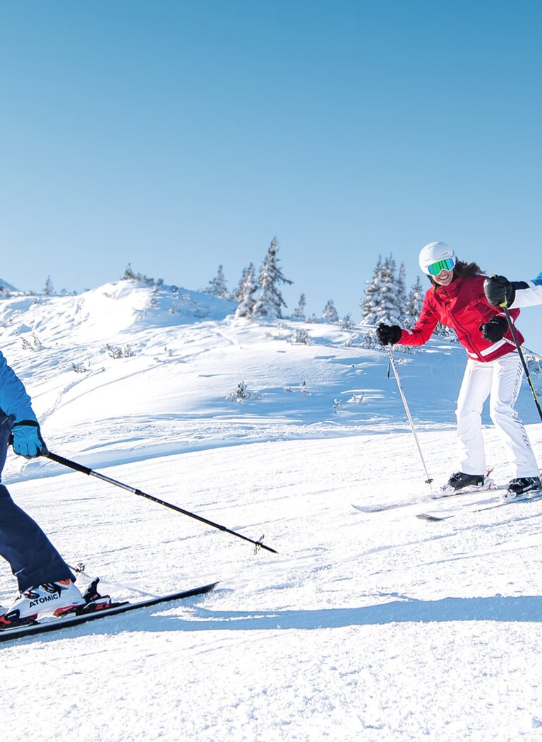 Group of skiers descending sunny slope together in Ski amadé | © Ski amadé GmbH Three skiers skiing side by side on a sunny, snowy slope with chairlifts in the background in Ski amadé. | © Ski amadé GmbH
