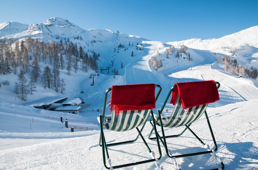 Zwei Liegestühle mit roten Decken stehen an einer verschneiten Skipiste vor Liften und schneebedeckten Bergen. | © Zauchensee Liftgesellschaft Benedikt Scheffer GmbH